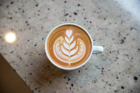 Frothy Espresso in a white mug with a heart, leaf and wave design in the froth.